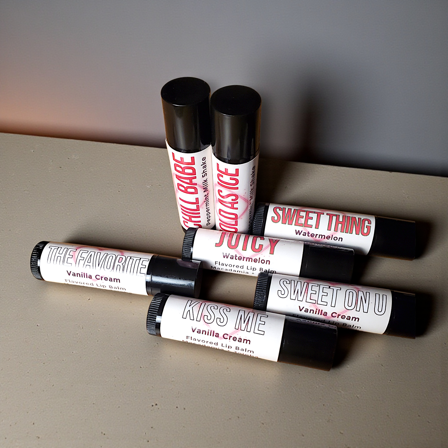 Collection of lip balm tubes with various flavors on a gray surface.