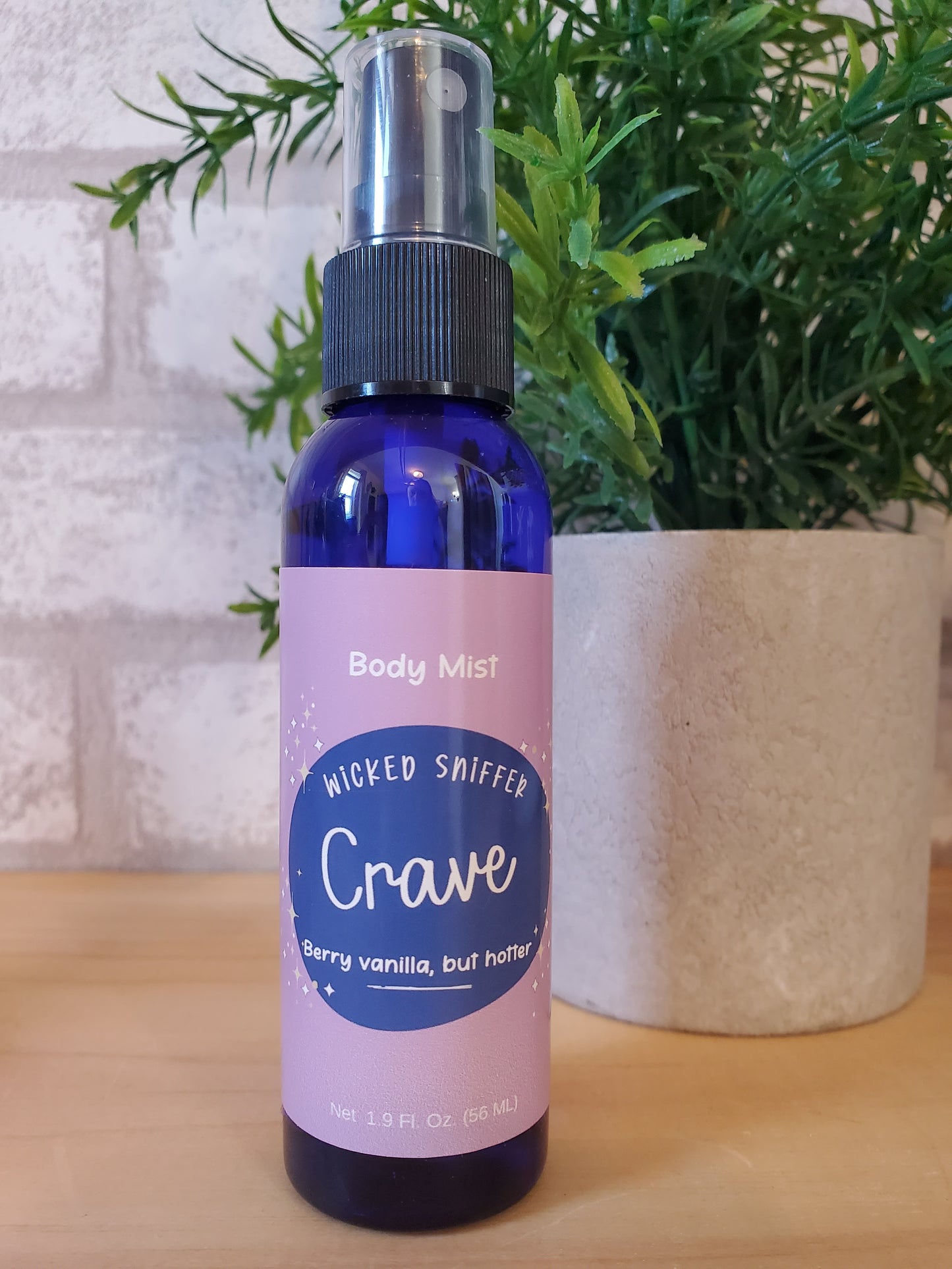 Blue and purple bottle of Crave body mist with a plant in the background