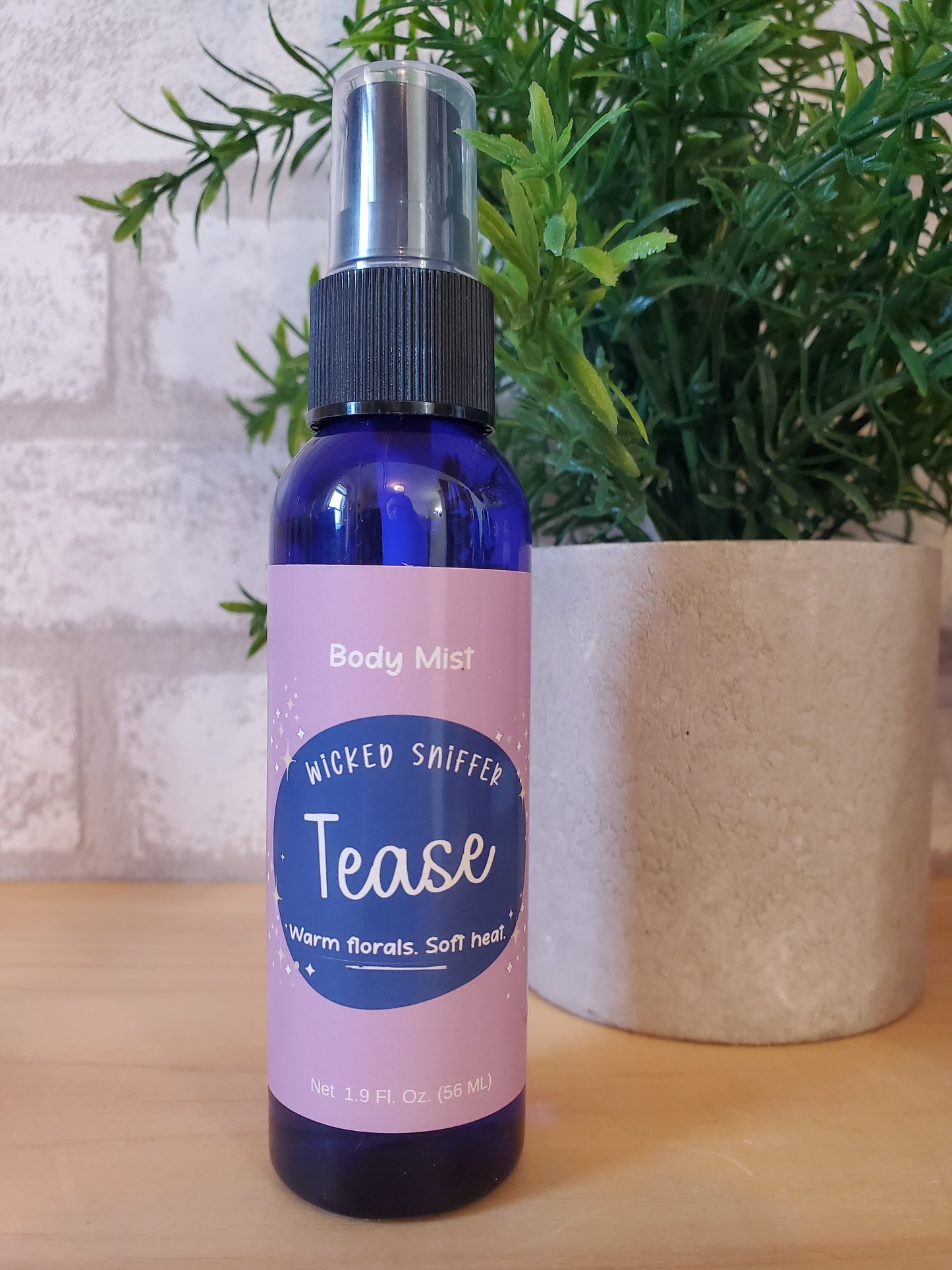 Bottle of 'Tease' body mist with pink label on a wooden surface