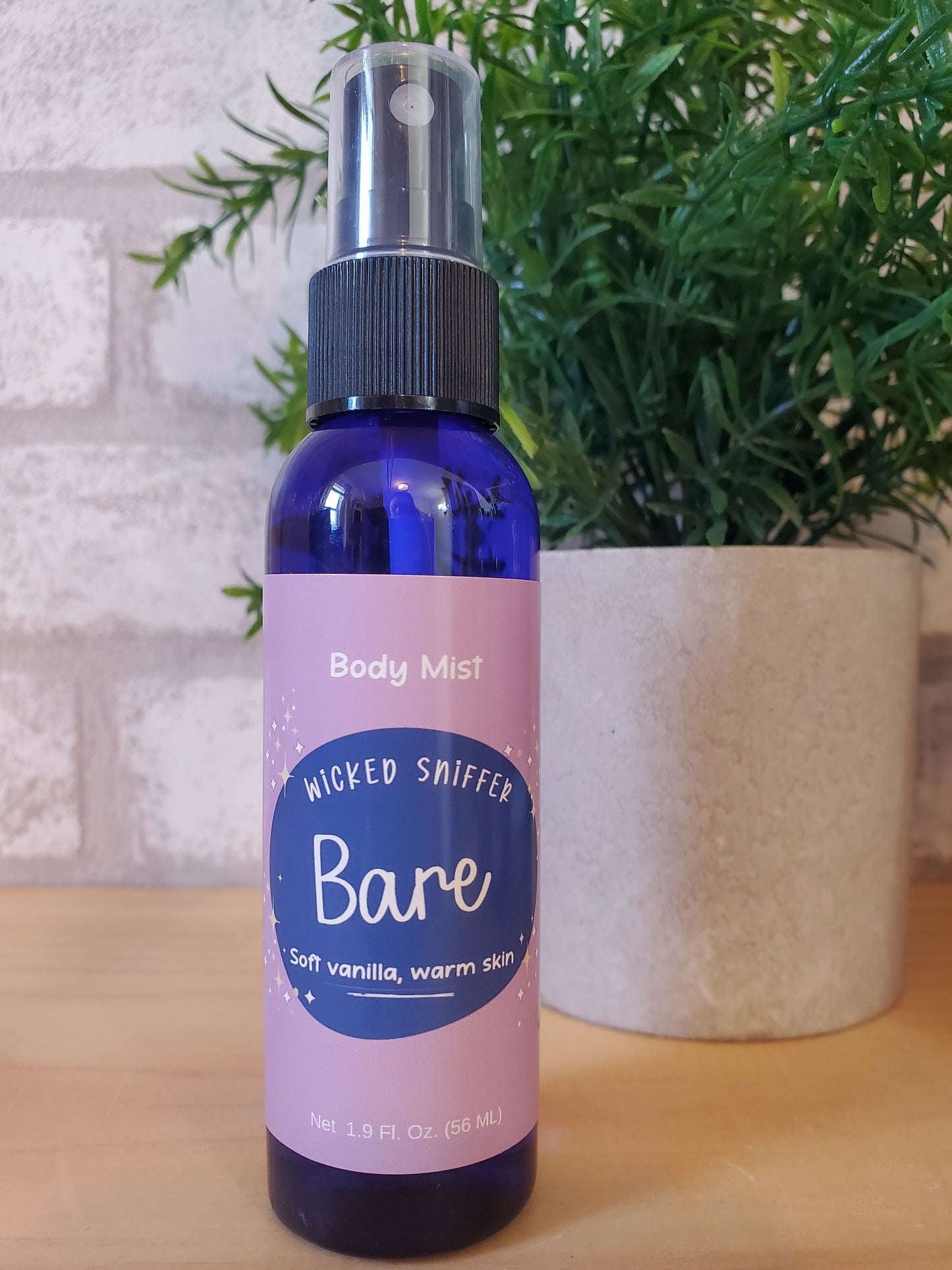 Bare body mist spray bottle on a wooden surface with greenery in the background