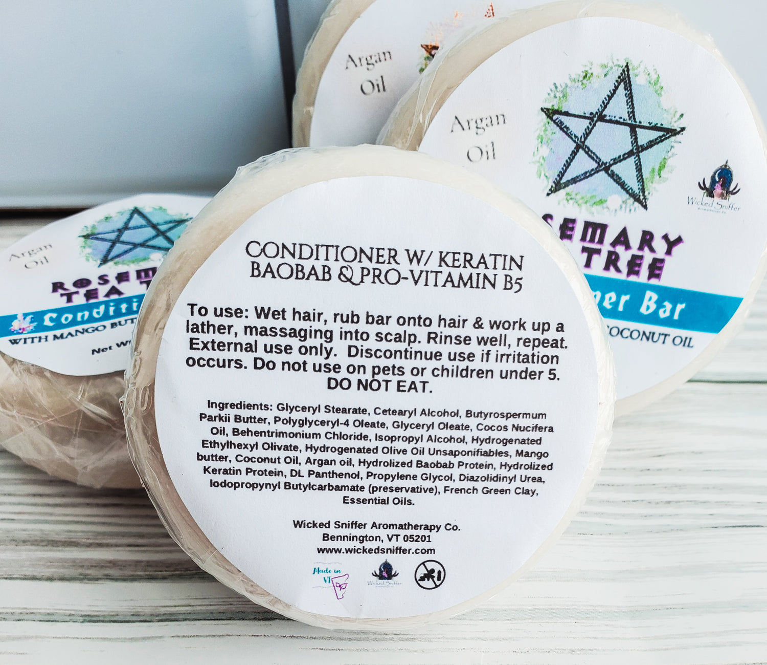 Photo of four round solid conditioner bars with white round labels, a blue band and pentagram. The back side of the label is facing forward listing ingredients and directions. 