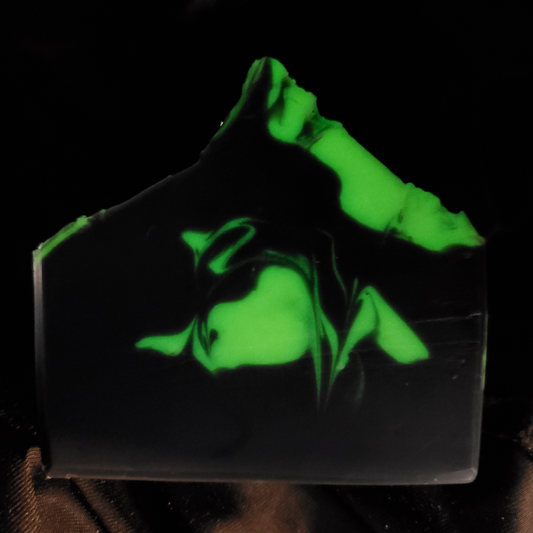 A rectangular bar of soap with a glossy black base and vibrant neon green marbled swirls, photographed against a dark background.
