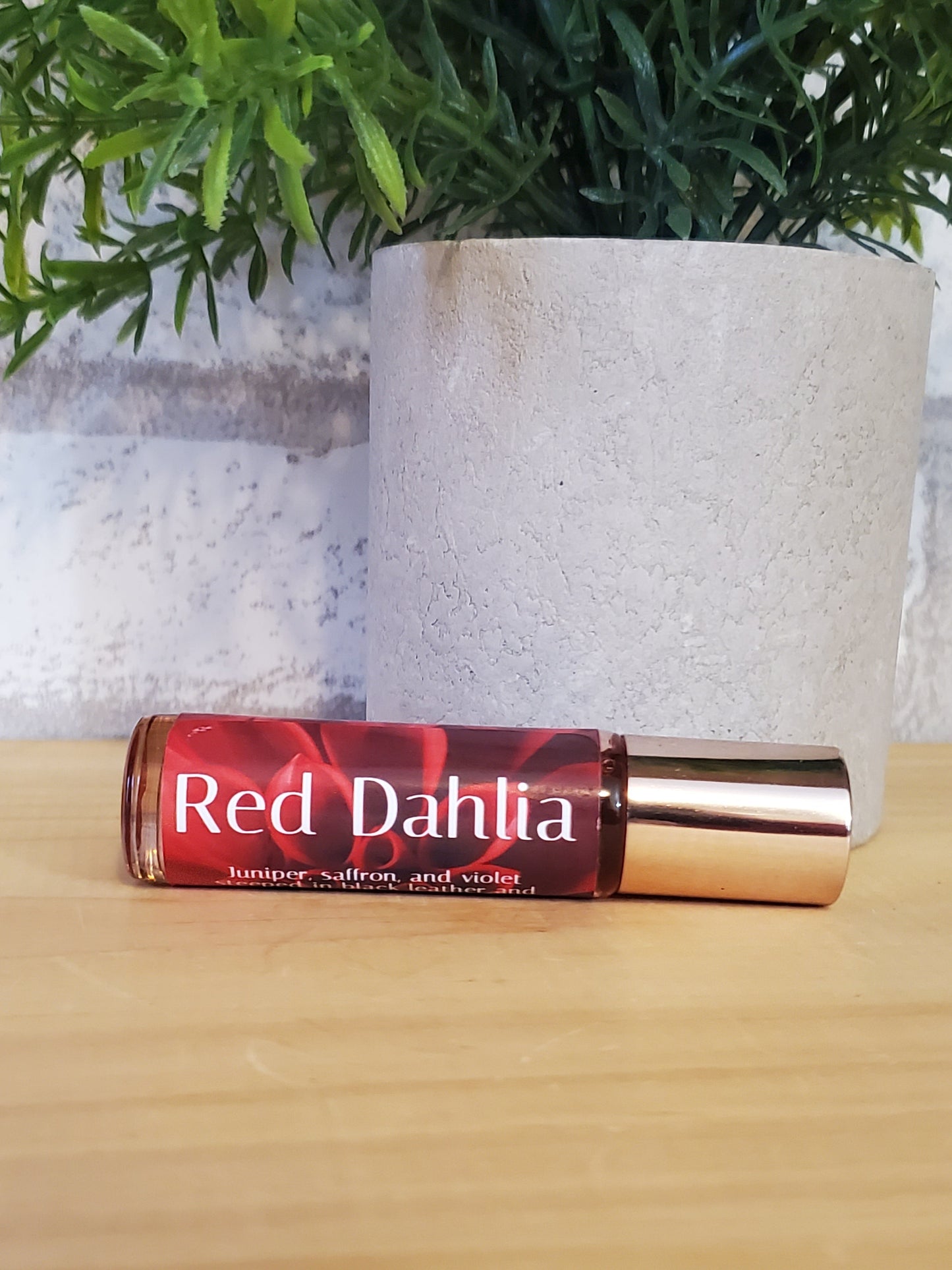 Red Dahlia perfume bottle on a textured surface with greenery