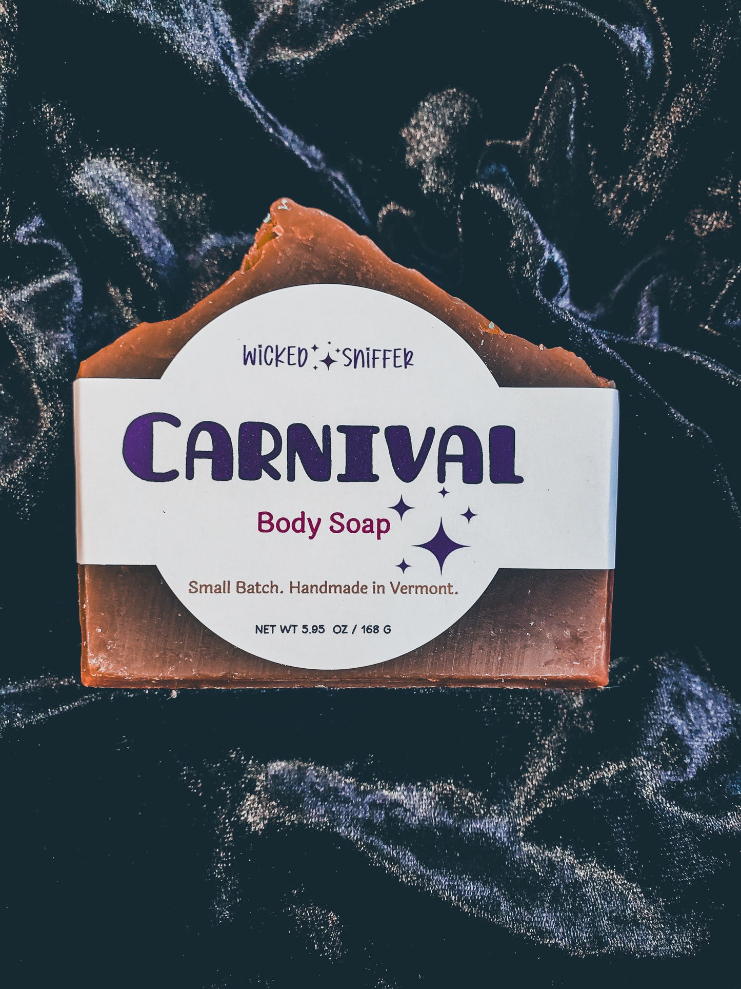 A rectangular bar of Wicked Sniffer Carnival Body Soap with a white paper label, displayed on a dark background