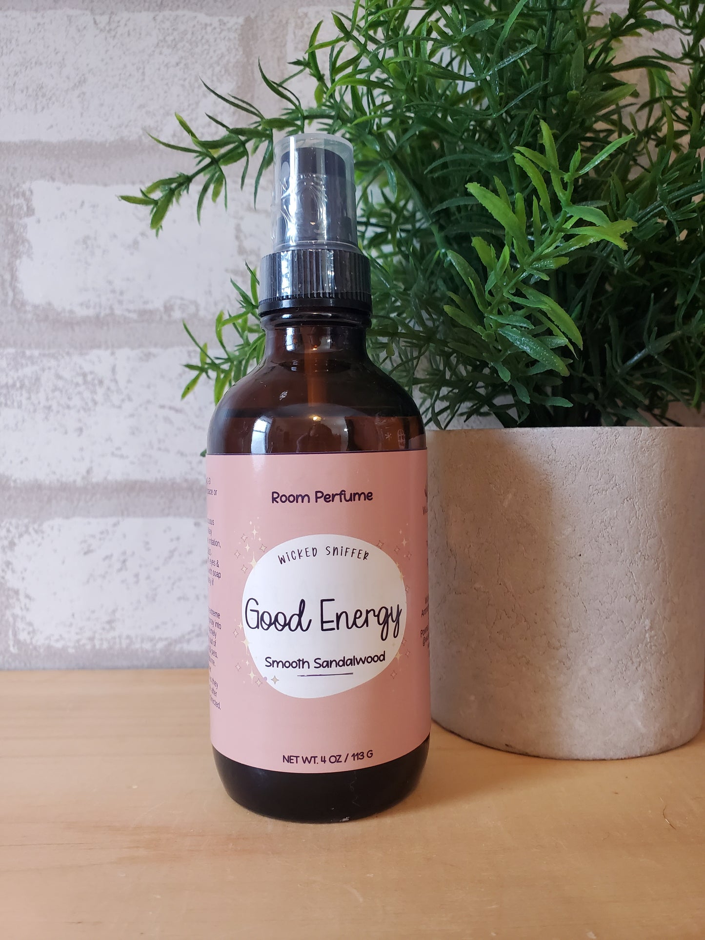 Bottle of room perfume with a pink label on a textured surface with greenery