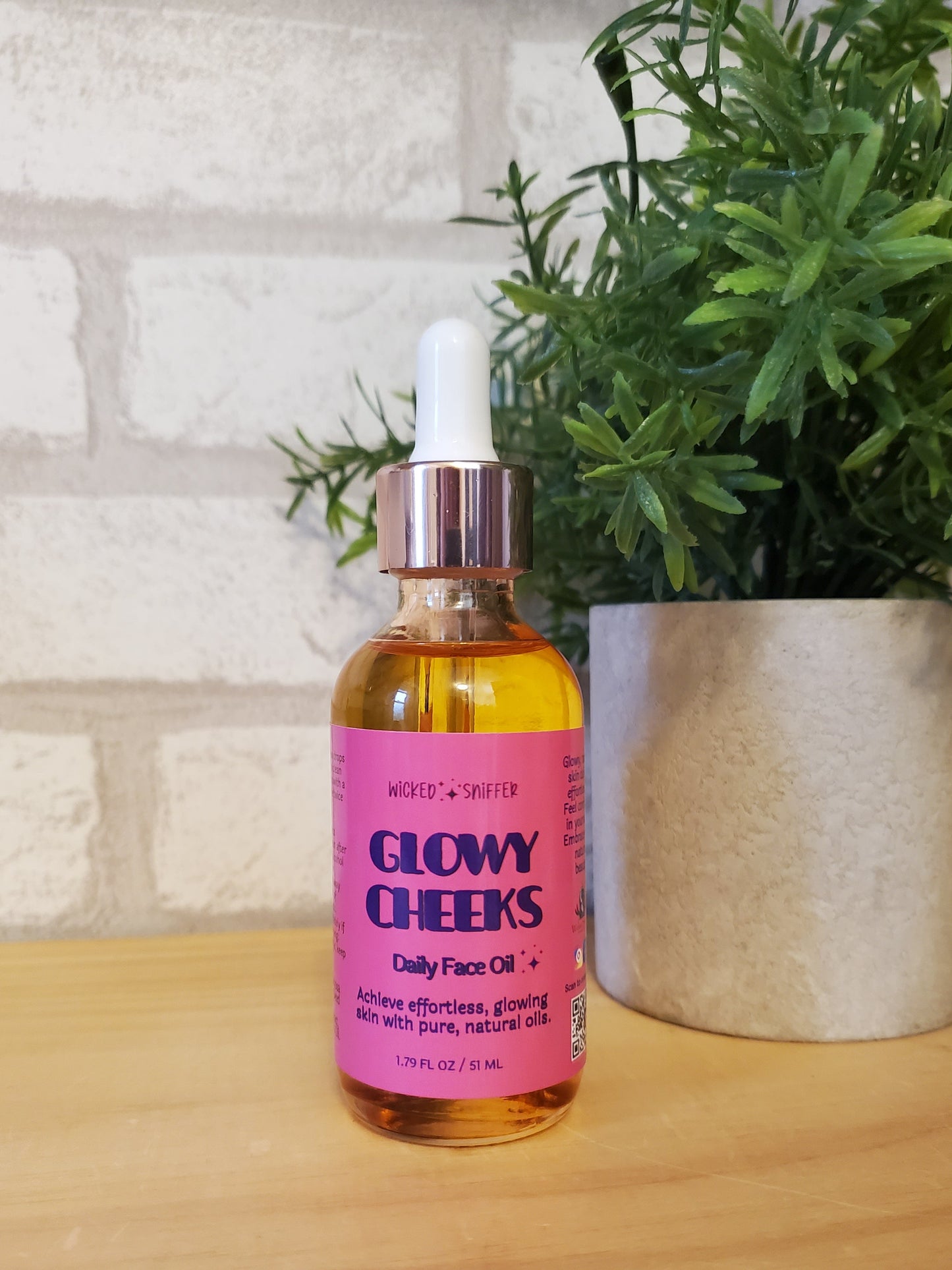 Bottle of 'Glowy Cheeks' facial oil on a wooden surface with a plant in the background