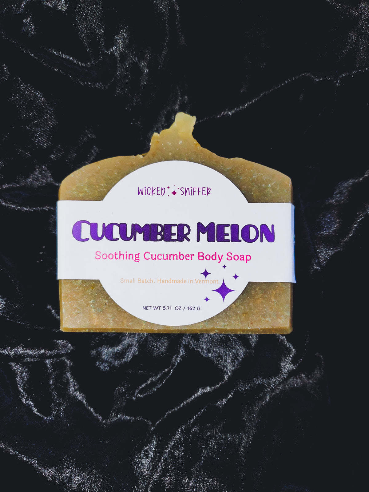A bar of Wicked Sniffer Cucumber Melon Soothing Cucumber Body Soap, resting on a black textured velvet fabric background.