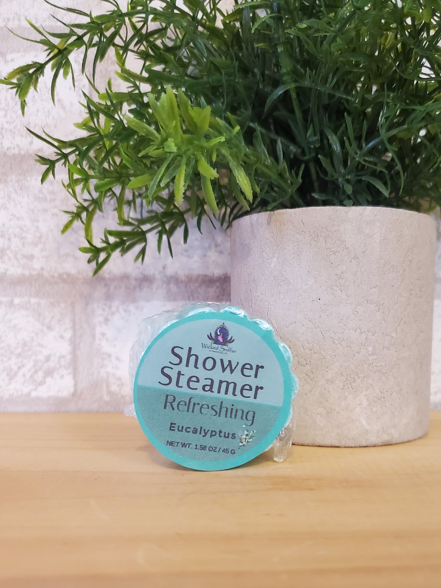 Shower steamer with a label on a towel next to greenery
