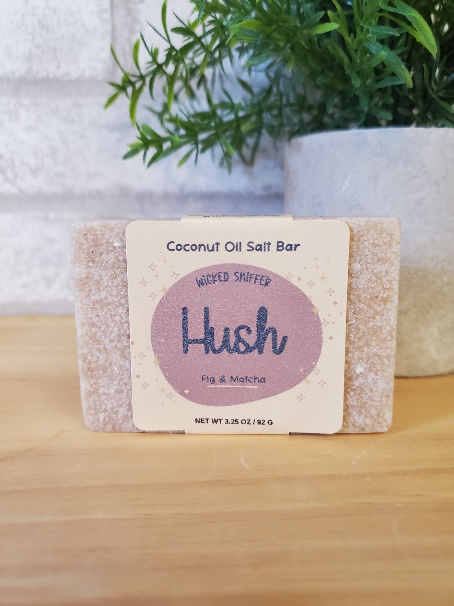 Coconut oil salt bar with 'Hush' branding on a wooden surface with greenery.