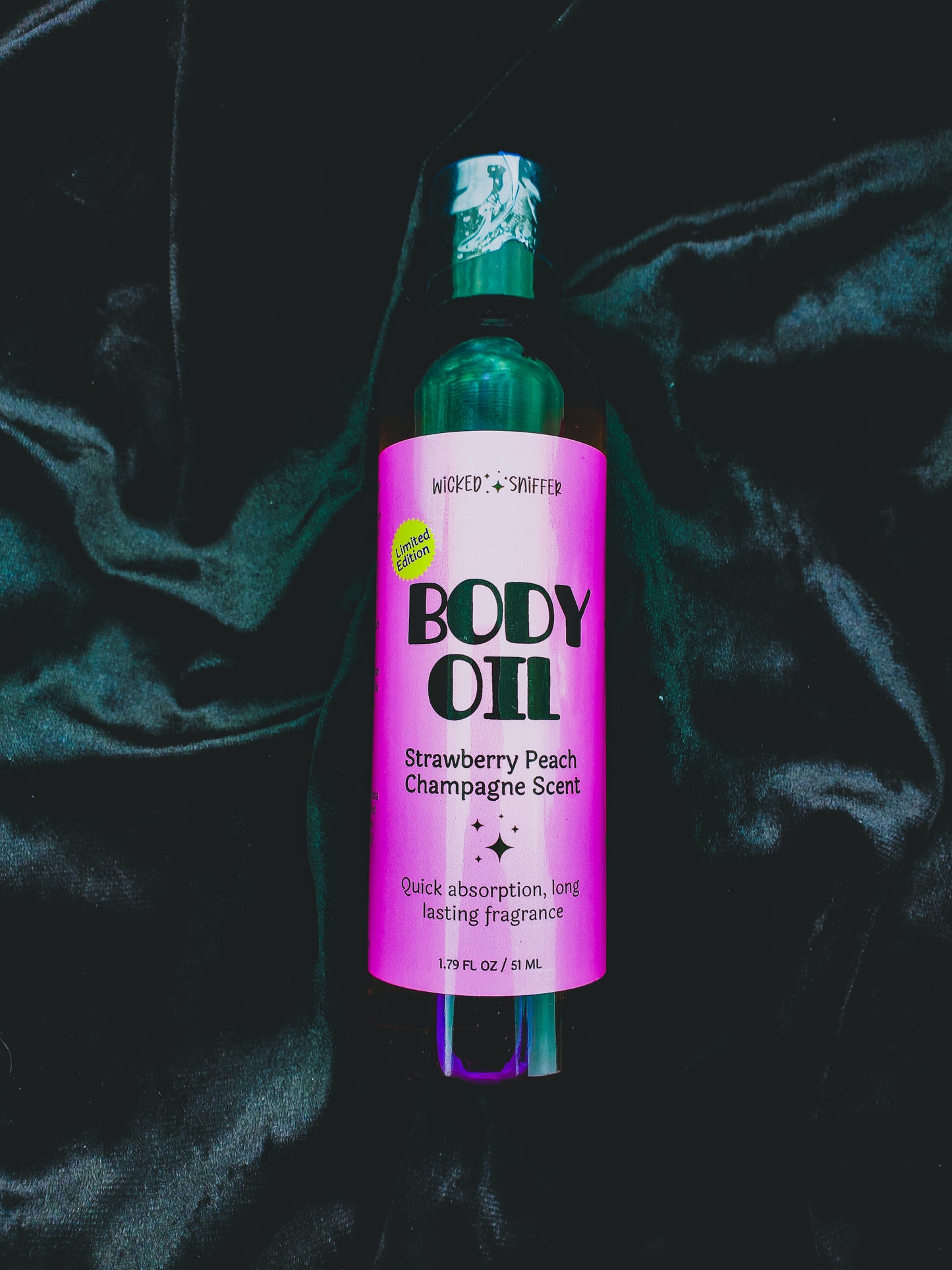 Bottle of body oil with a pink label on a dark fabric background