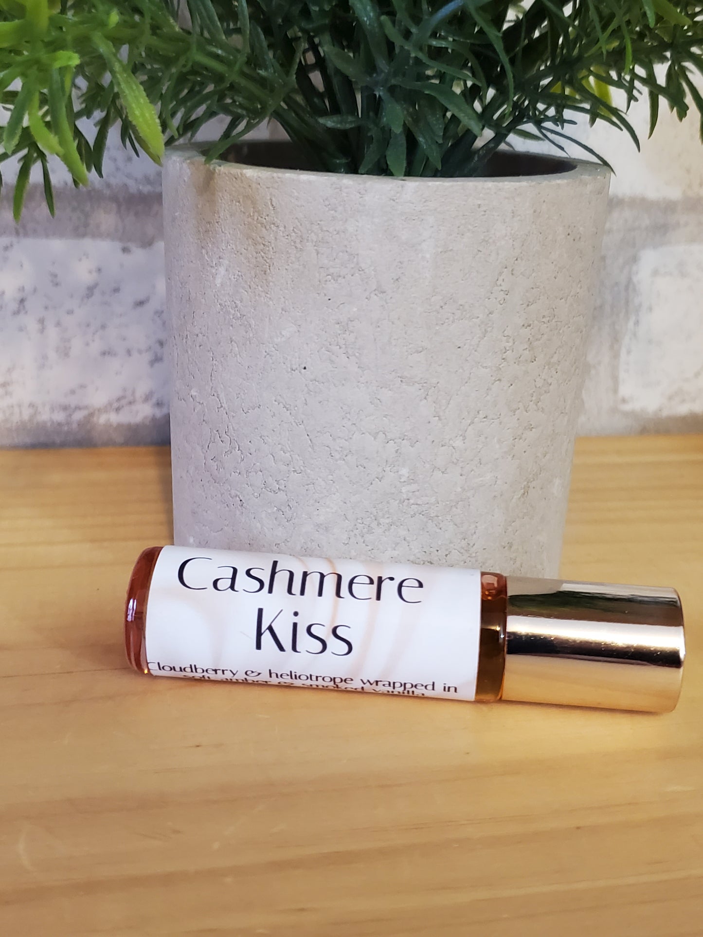 Roll-on bottle labeled 'Cashmere Kiss' on a textured surface with a plant in the background