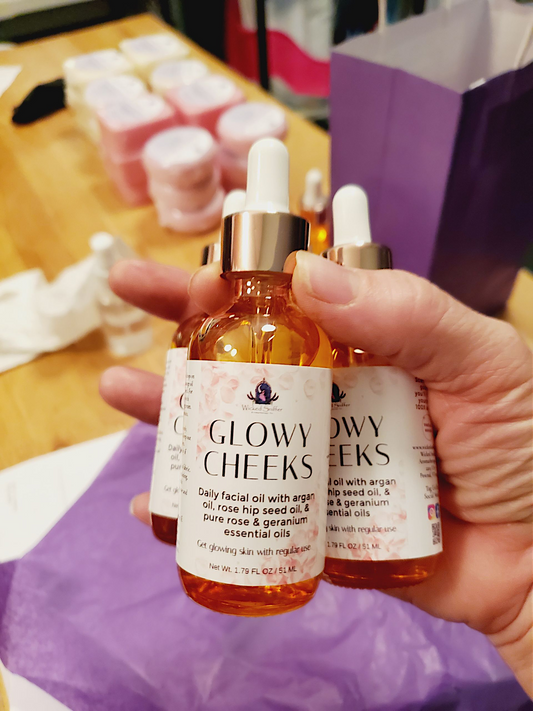 Hand holding two bottles of 'Glowy Cheeks' facial oil with a blurred background.