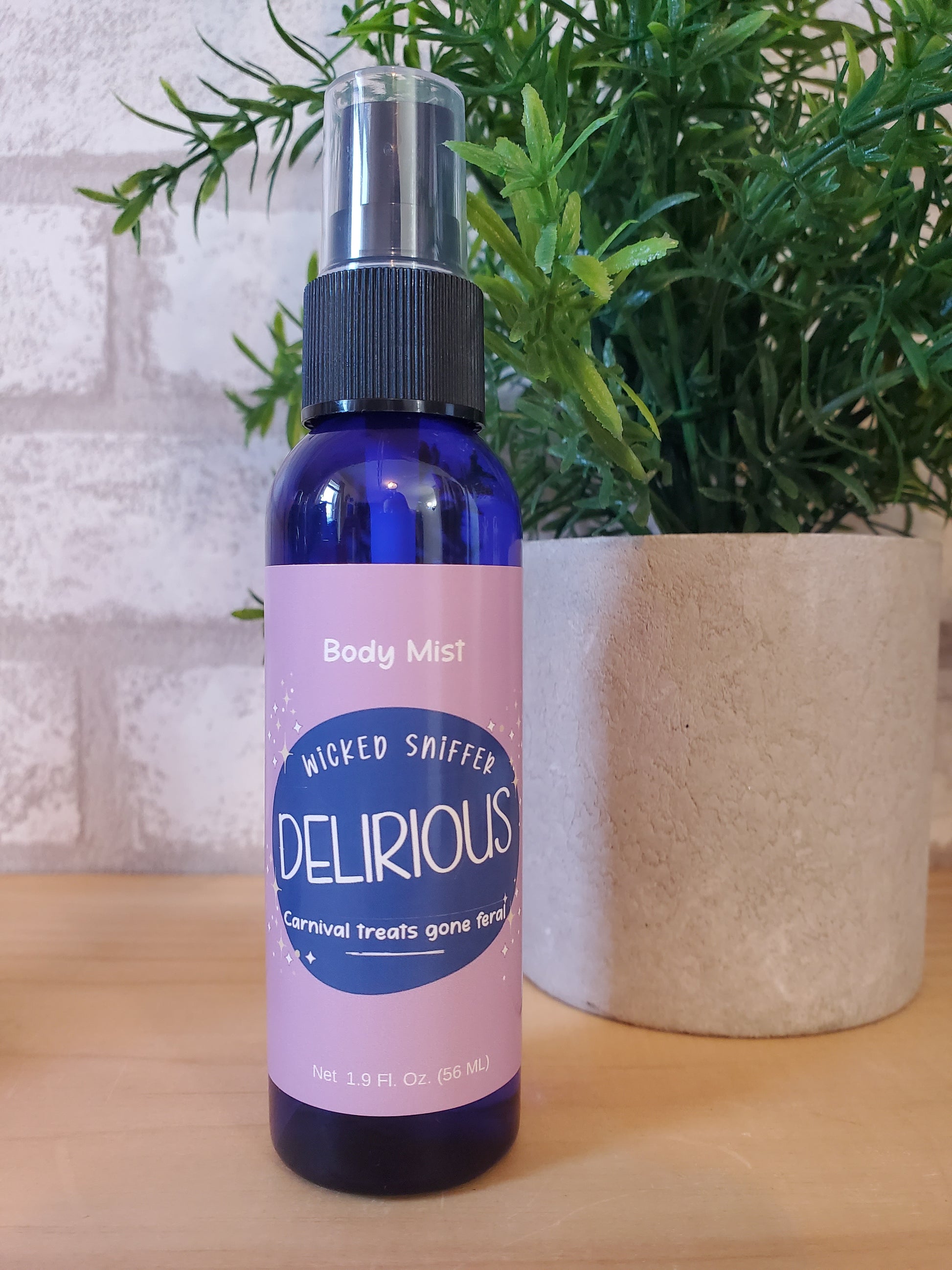 Delirious body mist bottle with pink label on a wooden surface with greenery
