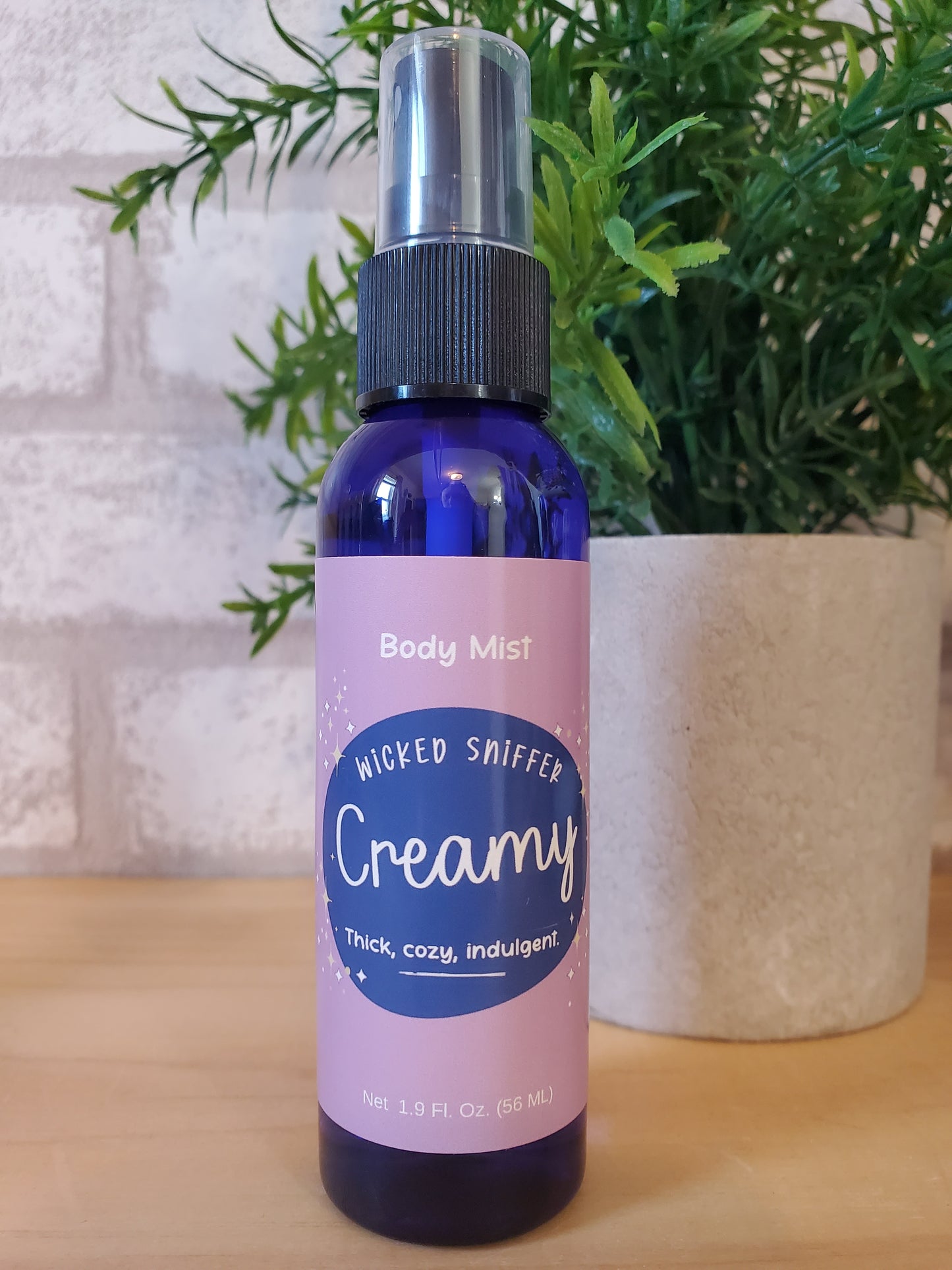 Body mist bottle labeled 'Creamy' with a plant in the background