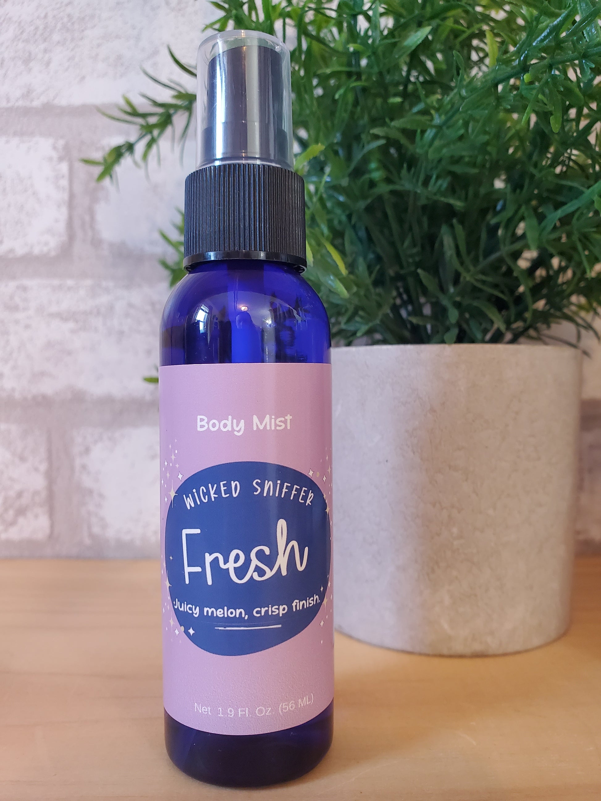 Body mist bottle labeled 'Wicked Sniffer' on a textured surface with greenery in the background