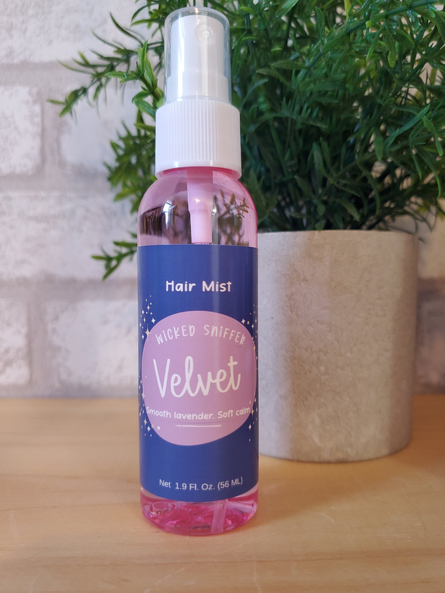 Hair mist bottle with pink and blue label on a wooden surface