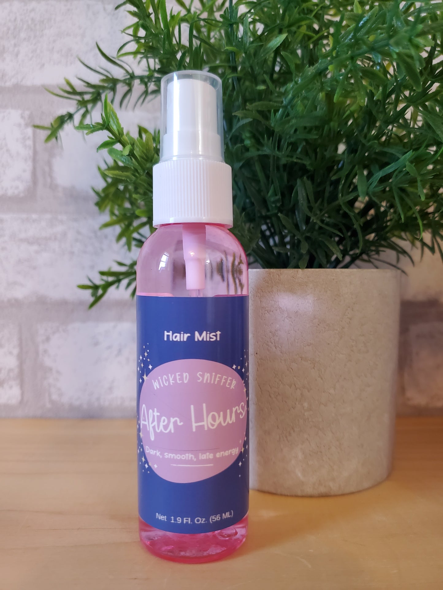 Hair mist bottle with pink label on a wooden surface next to green plants