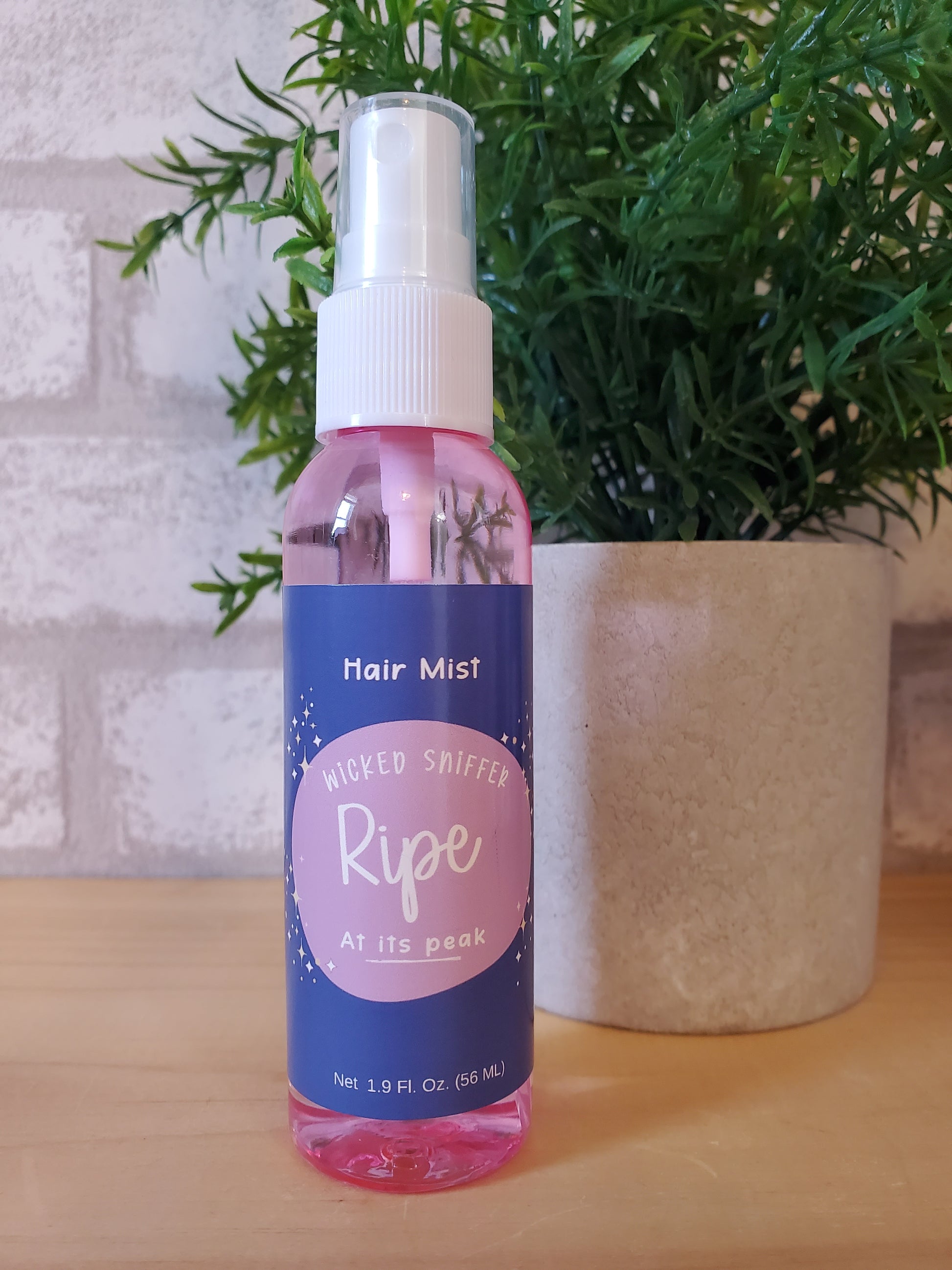 Ripe hair mist bottle on a textured surface with greenery in the background