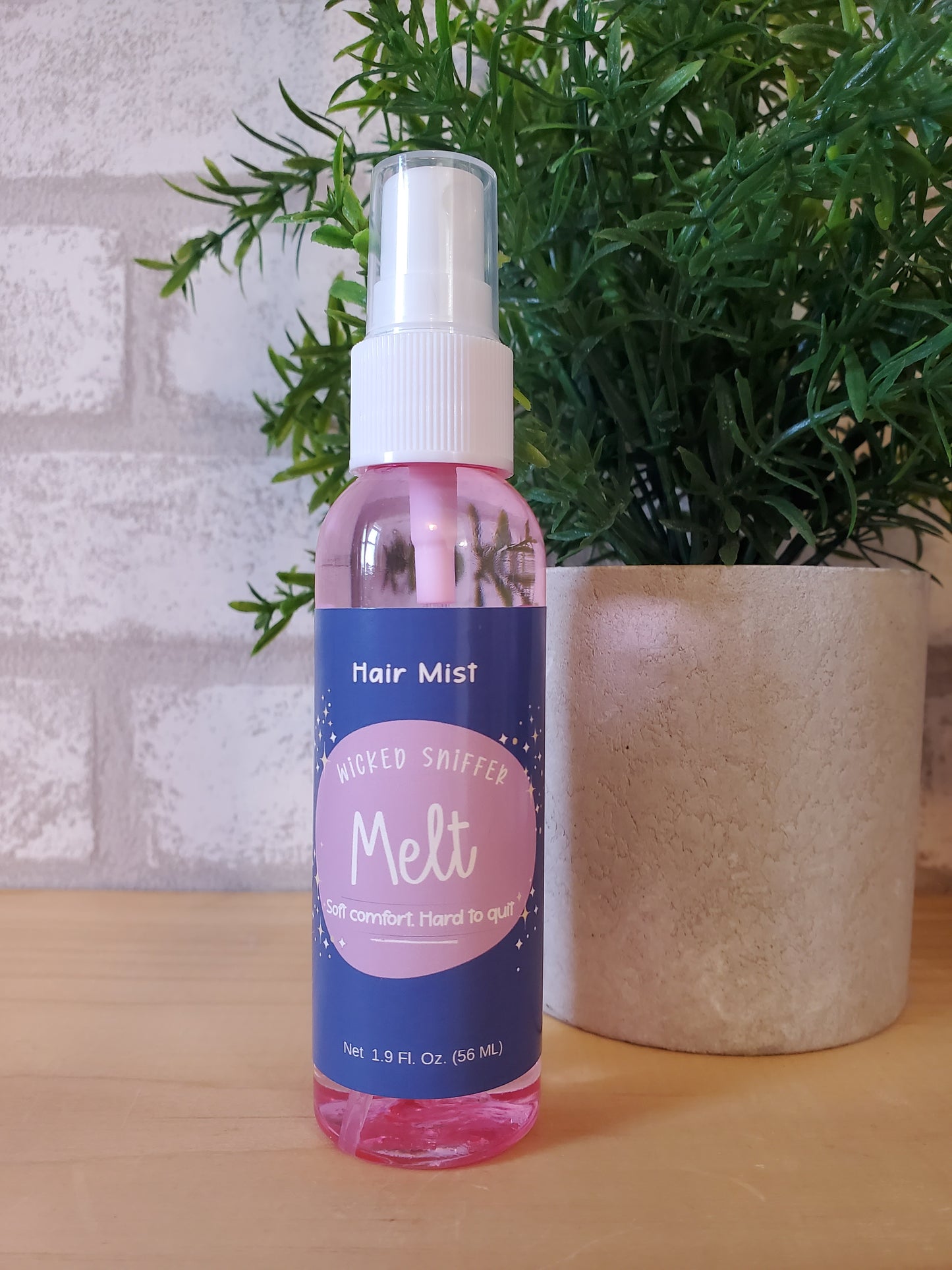 Spray bottle with pink and blue label on a wooden surface with greenery in the background