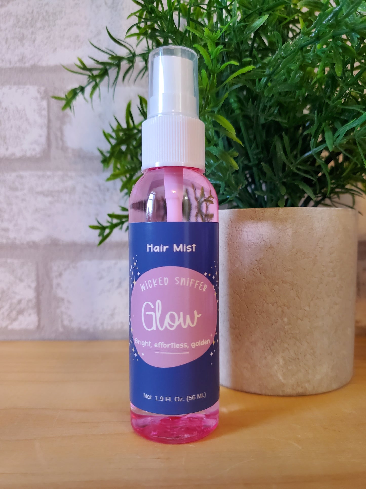 Hair mist bottle labeled 'Glow' on a textured surface with greenery in the background