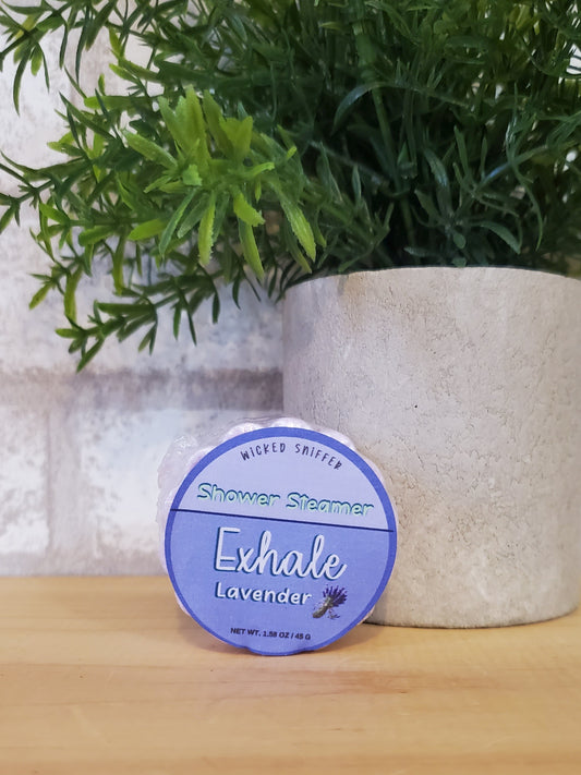 Exhale lavender shower steamer on a white surface with greenery and wooden background