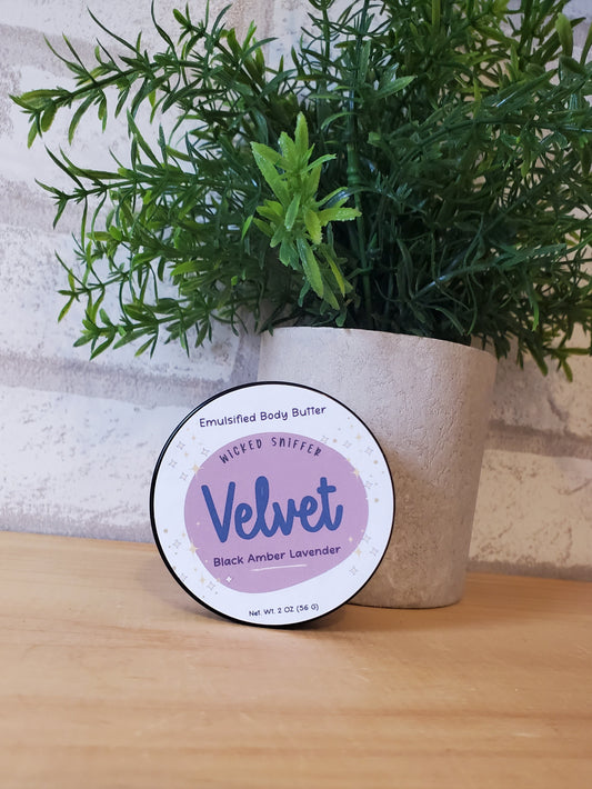Round body butter container labeled 'Velvet' with a plant and wooden surface in the background
