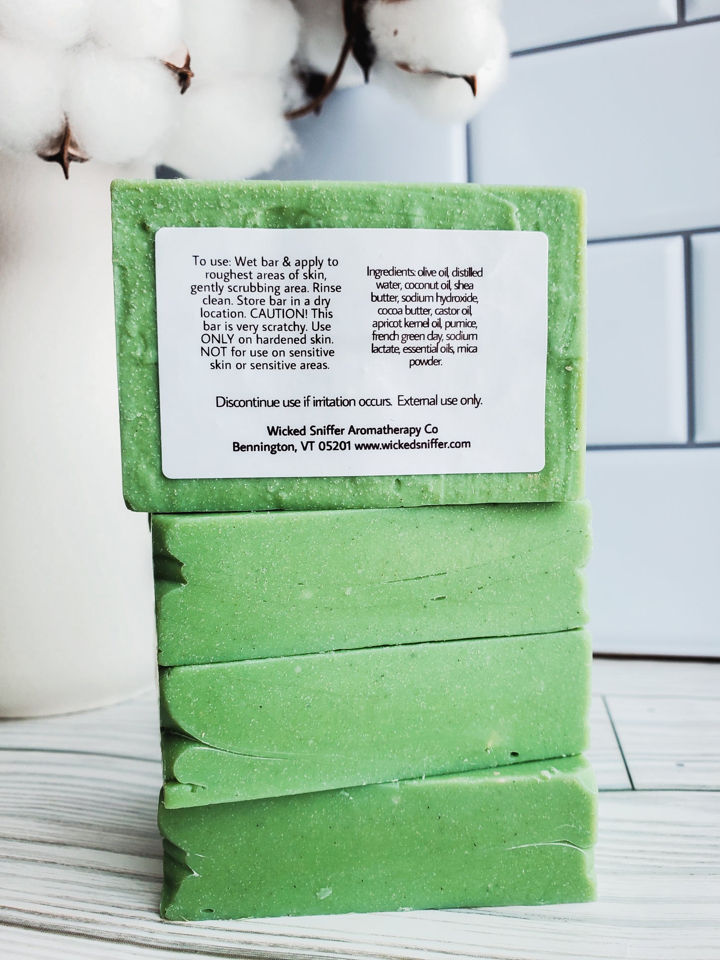 Picture of 4 green bars of soap stacked high with a white rectangular label with the back label facing out with directions and ingredients. 