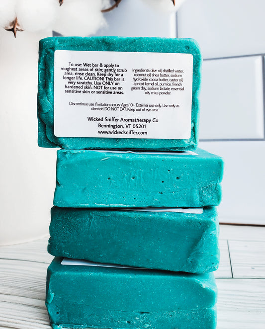Picture of 4 blue bars of soap stacked high with a white rectangular label with the backside facing out with ingredients and directions. 
