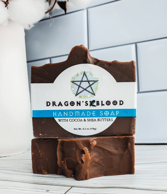 Picture of two brown bars of soap, one stacked on top of one lying flat, with a white wrap around label with a blue stripe, a pentagram, a small dragon and black lettering.