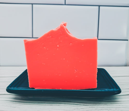 Photo of an orange bar of soap standing up in a blue soap dish with a white tile background. 