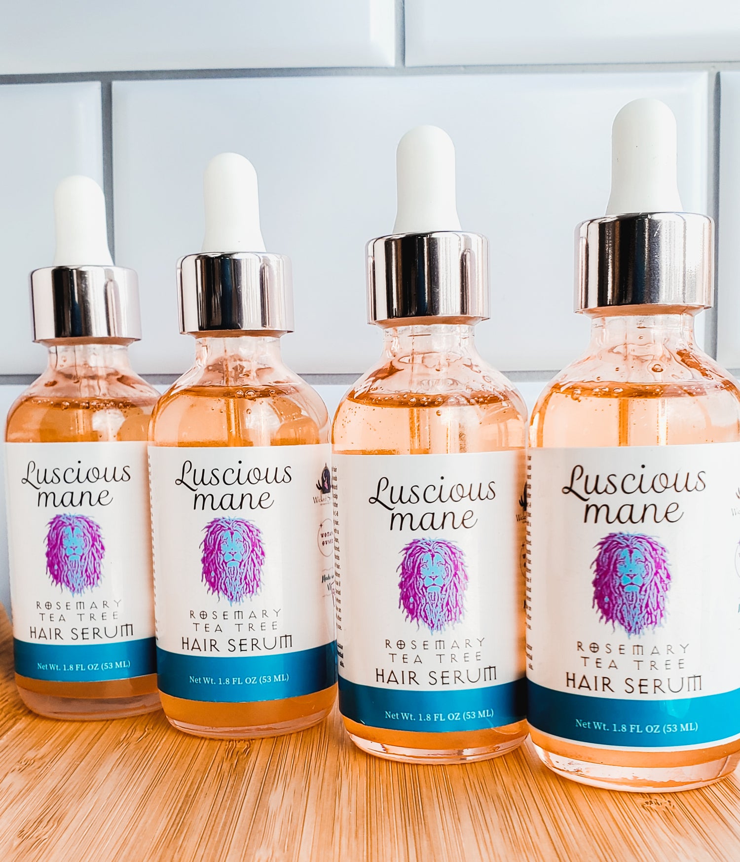 Photo of 4 orange bottles with white labels with a purple and blue lions that says luscious mane rosemary Tea Tree hair serum.