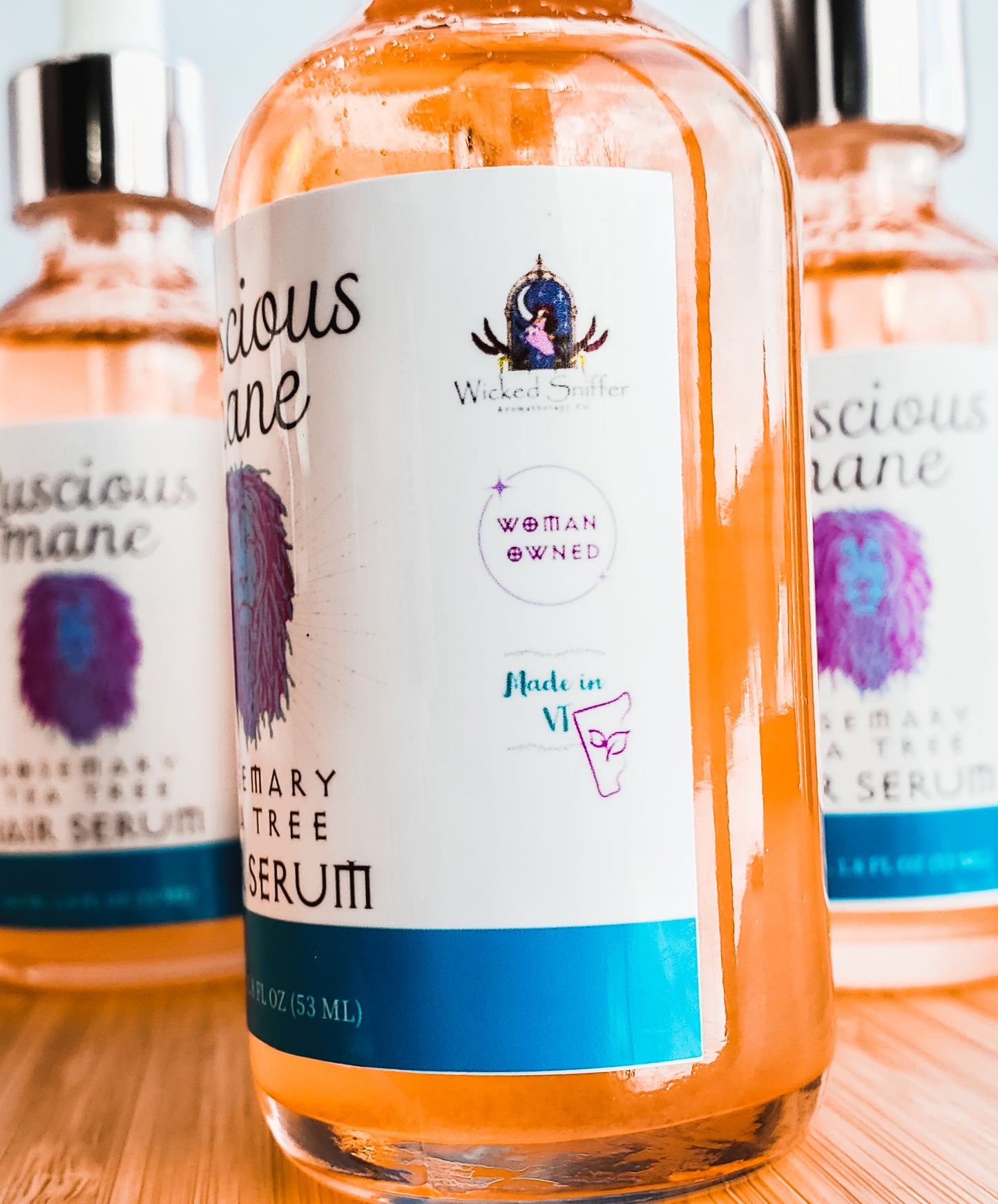Photo of 3 orange bottles with white labels with a purple and blue lions that says luscious mane rosemary Tea Tree hair serum.