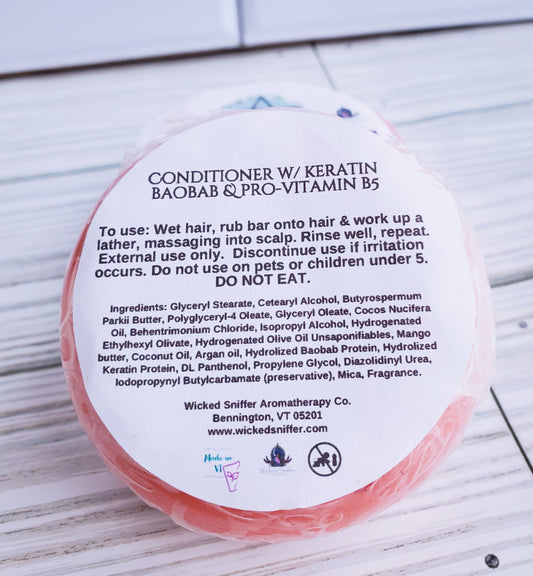 Picture of the back of a round solid red conditioner bar with a white label that has directions and ingredients. 