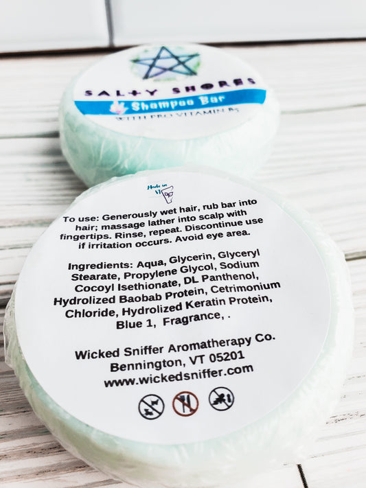 Photo of two round solid shampoo bars with a white label. The back label is facing out with directions and ingredients. 