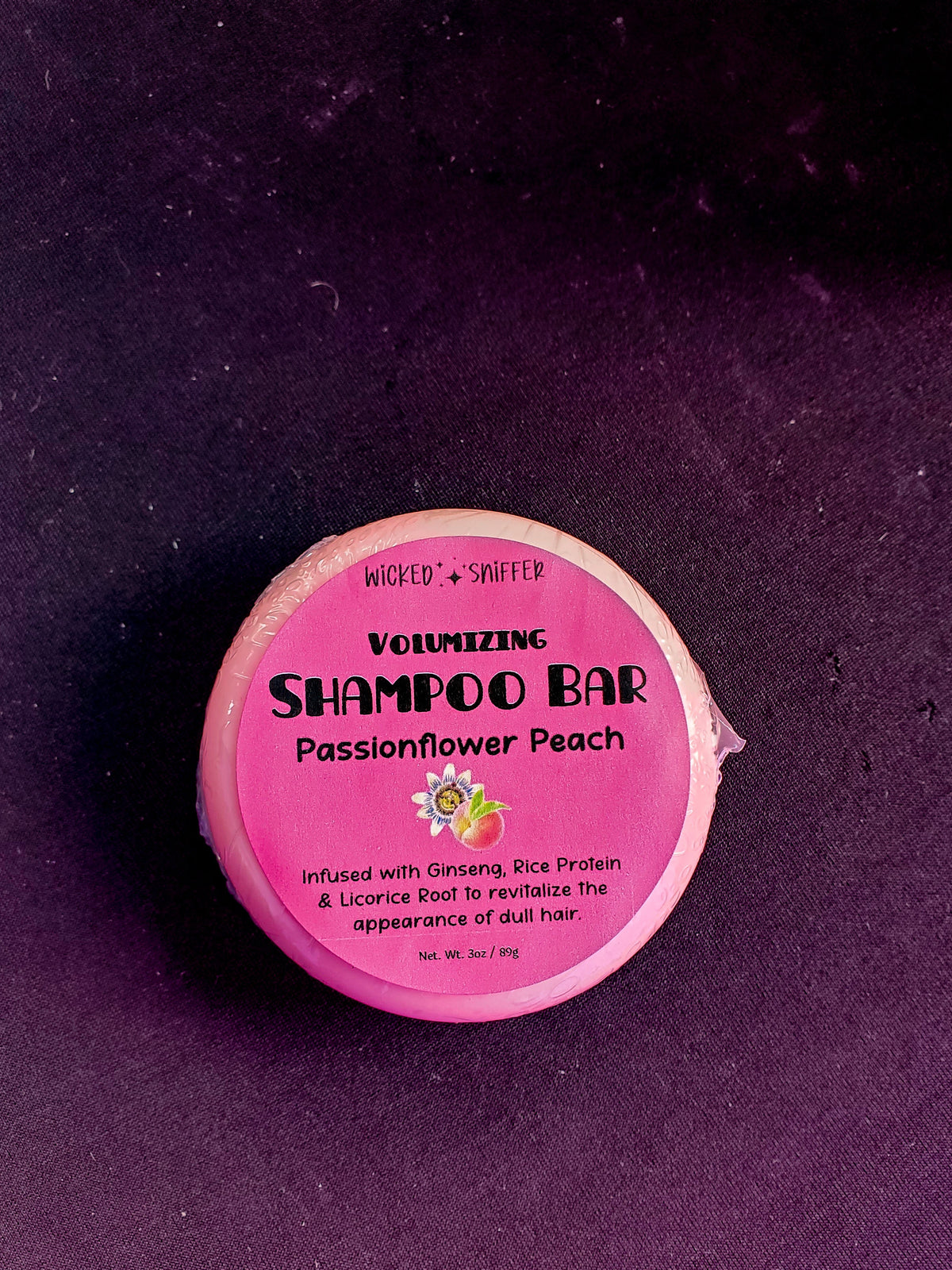 A shampoo bar wrapped in plastic on a dark background.