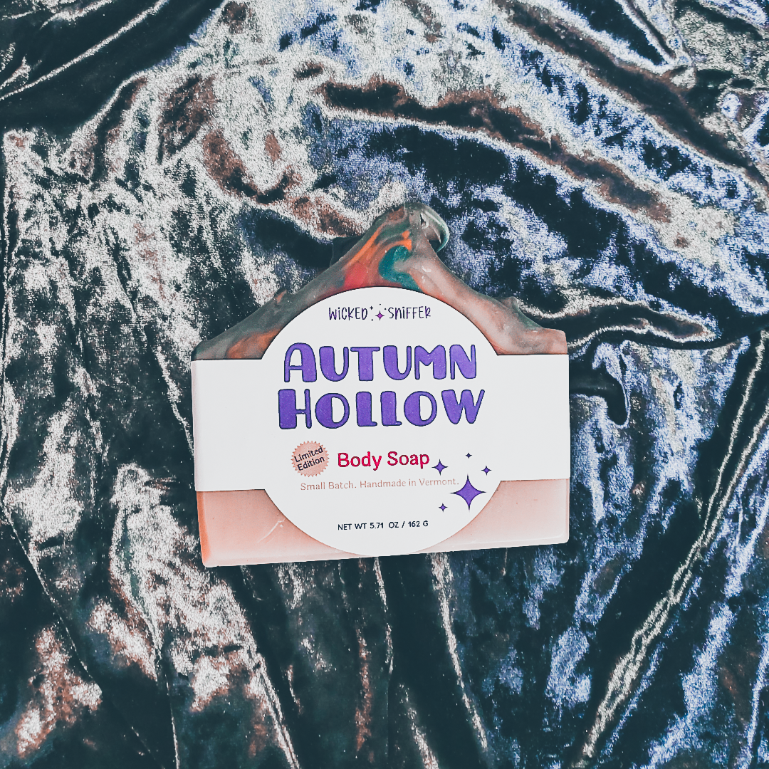 A packaged bar of body soap labeled 'Autumn Hollow' by Wicked Sniffer, placed on a dark surface with white and silver veining. The soap package is white with purple lettering.