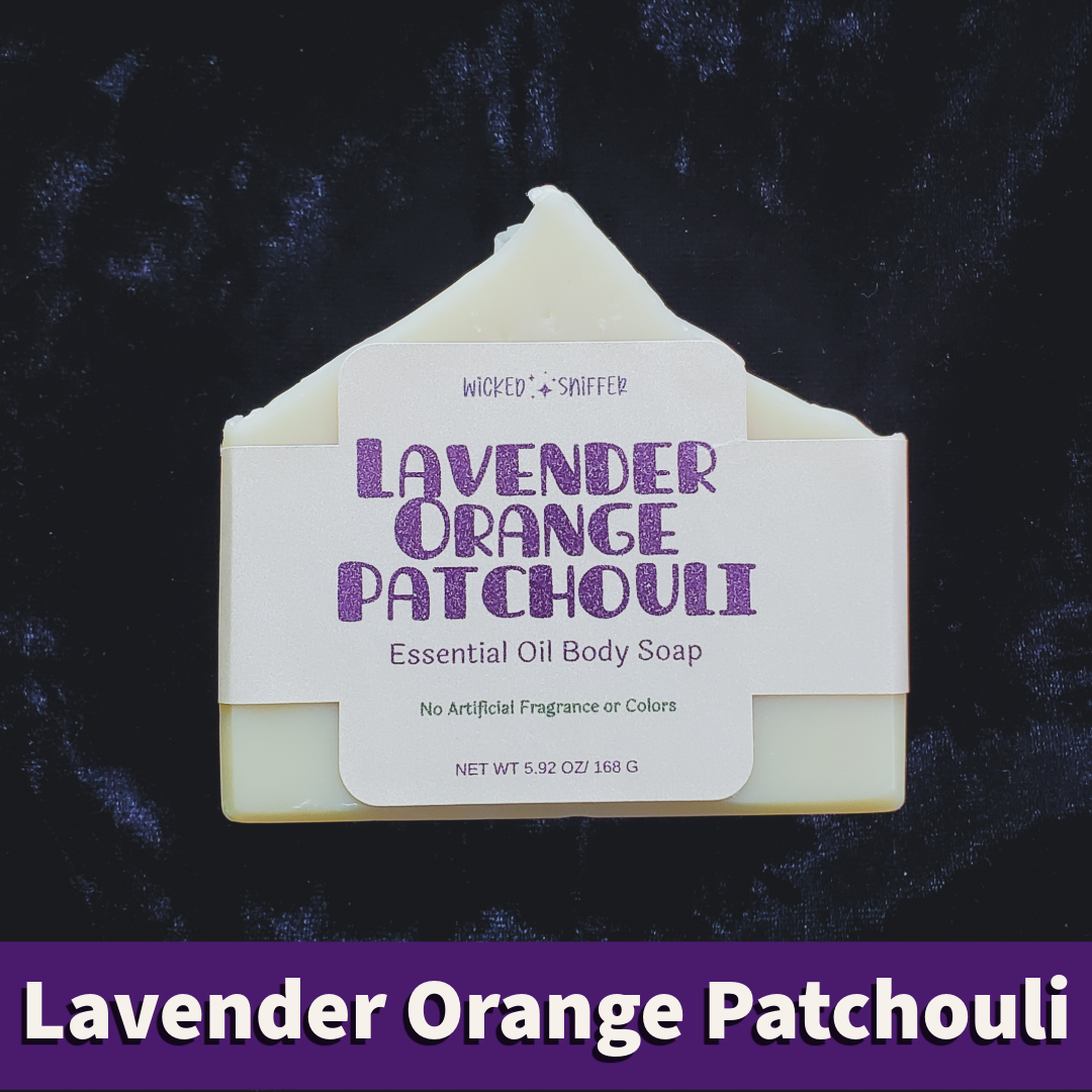 A single bar of Lavender Orange Patchouli Essential Oil Body Soap is centered against a dark textured background. The soap bar is pale cream with a white paper label featuring purple text.
