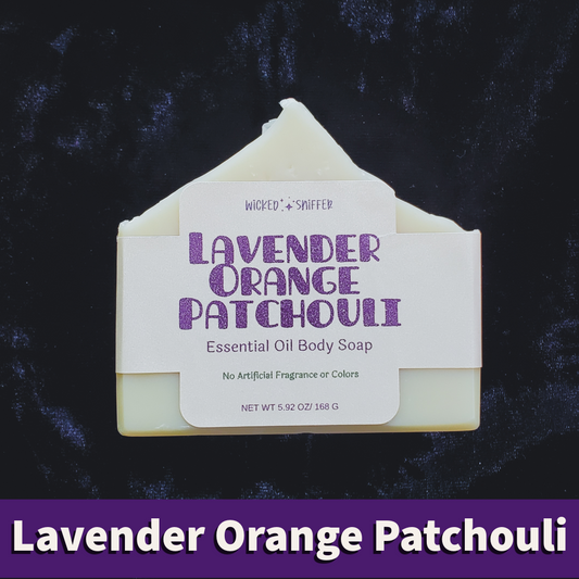 A single bar of Lavender Orange Patchouli Essential Oil Body Soap is centered against a dark textured background. The soap bar is pale cream with a white paper label featuring purple text.