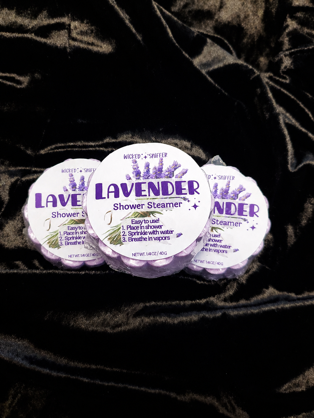 Three lavender shower steamers on a dark textured surface