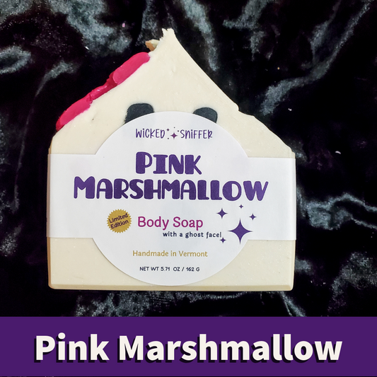 A house-shaped body soap bar labeled 'Pink Marshmallow' by Wicked Sniffer, shown on a dark plush velvet background with a purple text banner at the bottom reading 'Pink Marshmallow'. The soap has a cream body, purple lettering, a pink top section, and a ghost face detail peeking up from the label.