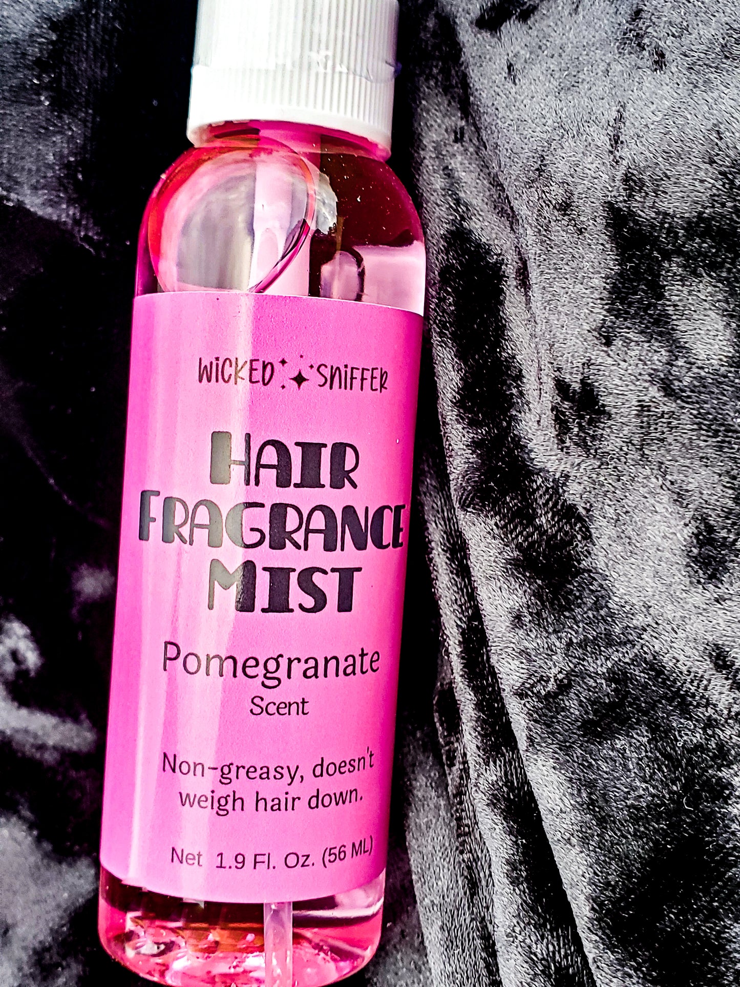 Pink hair fragrance mist bottle labeled 'Wicked Sniffer' on a textured black and gray background