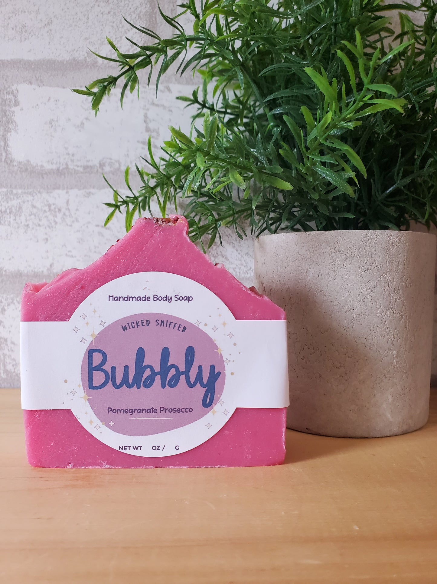Pink soap bar with a white label on a textured surface with greenery
