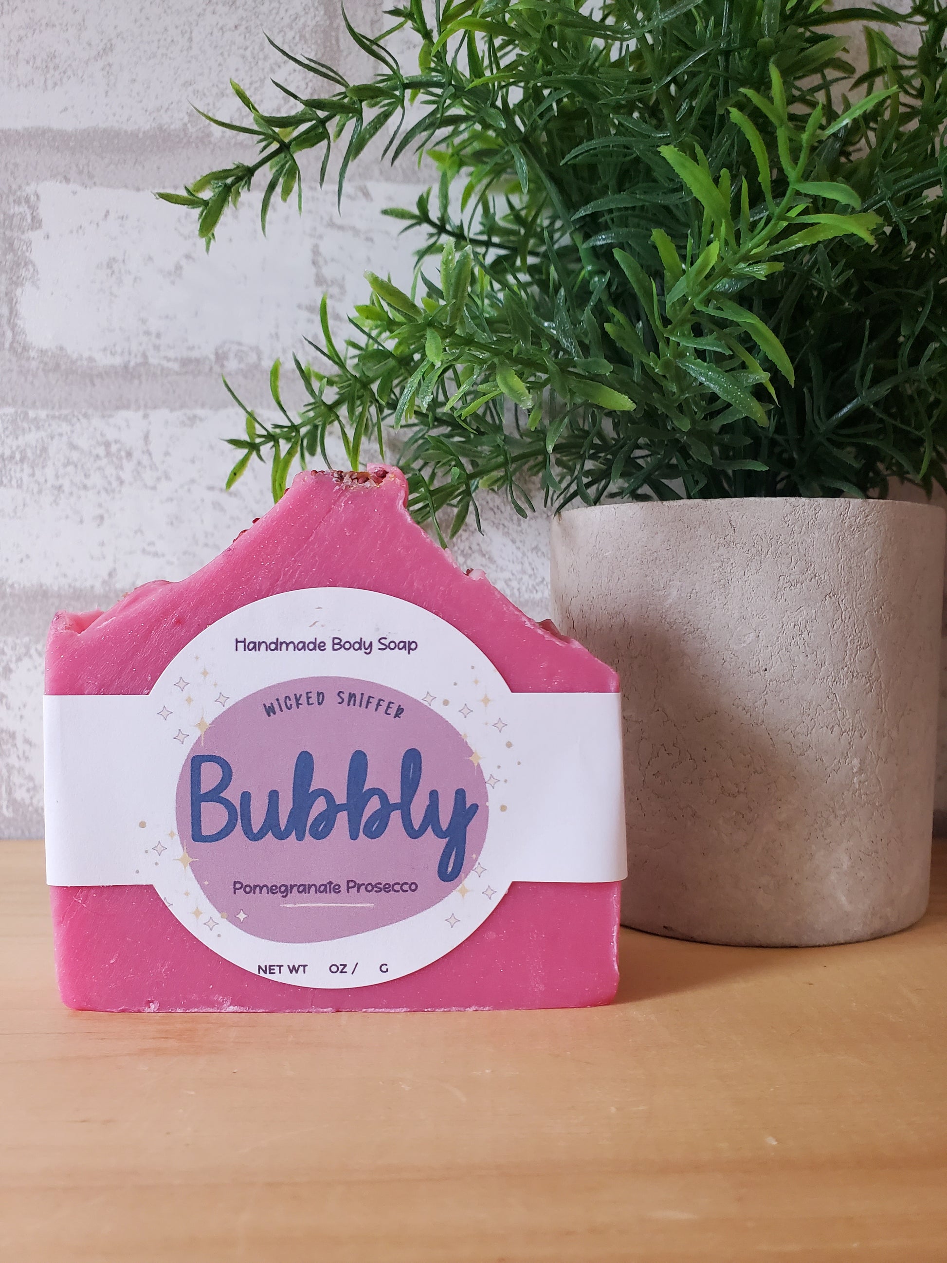 Pink soap bar with a white label on a textured surface with greenery