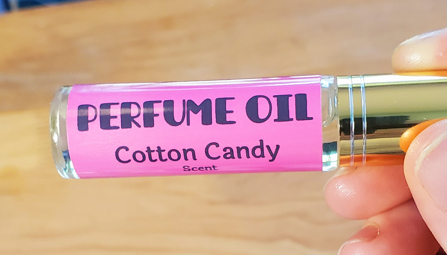 Perfume oil vial labeled 'Cotton Candy' with a pink label on a wooden surface.