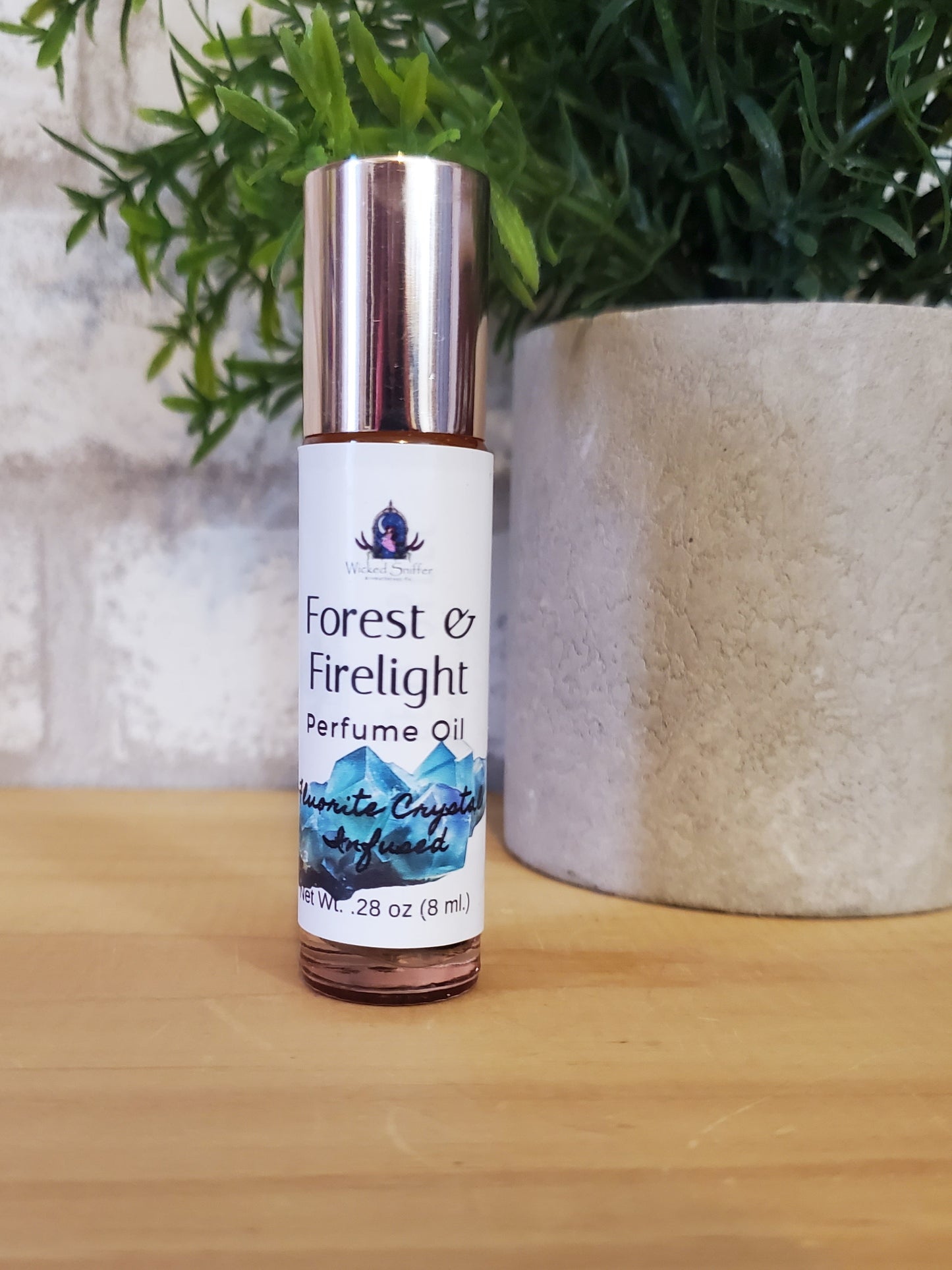 Perfume oil bottle labeled 'Forest Firelight' on a wooden surface with greenery.