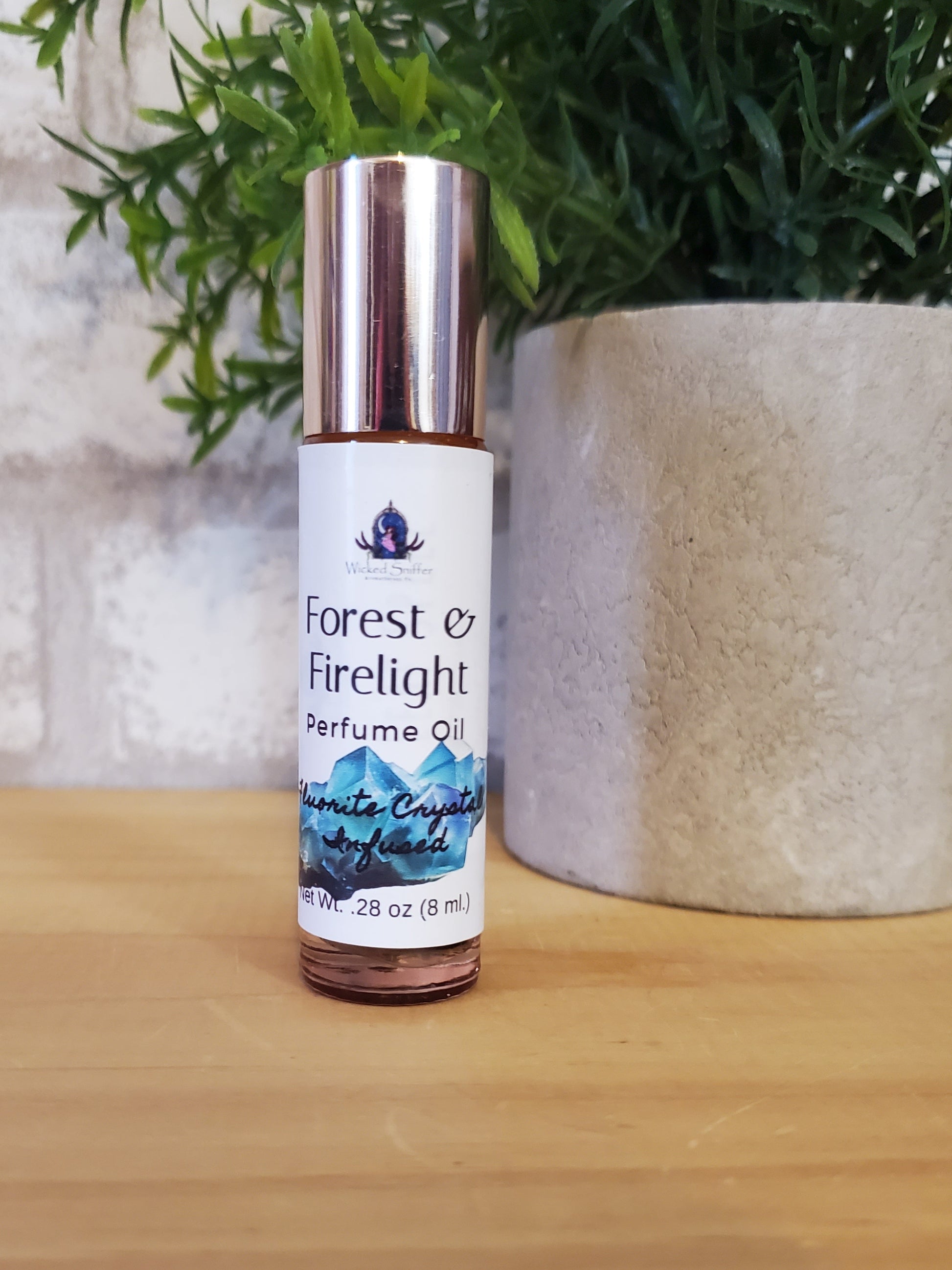 Perfume oil bottle labeled 'Forest Firelight' on a wooden surface with greenery.