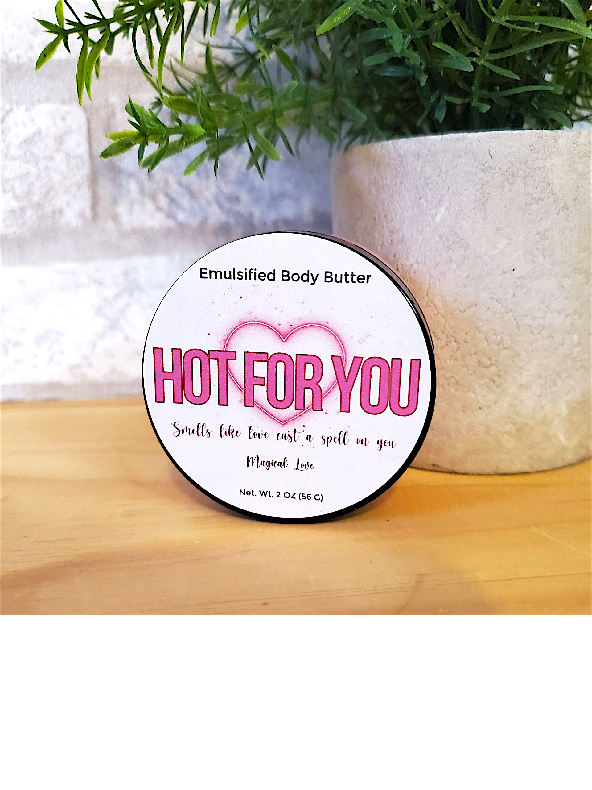 Body butter container labeled 'Hot for You' on a wooden surface with a plant in the background