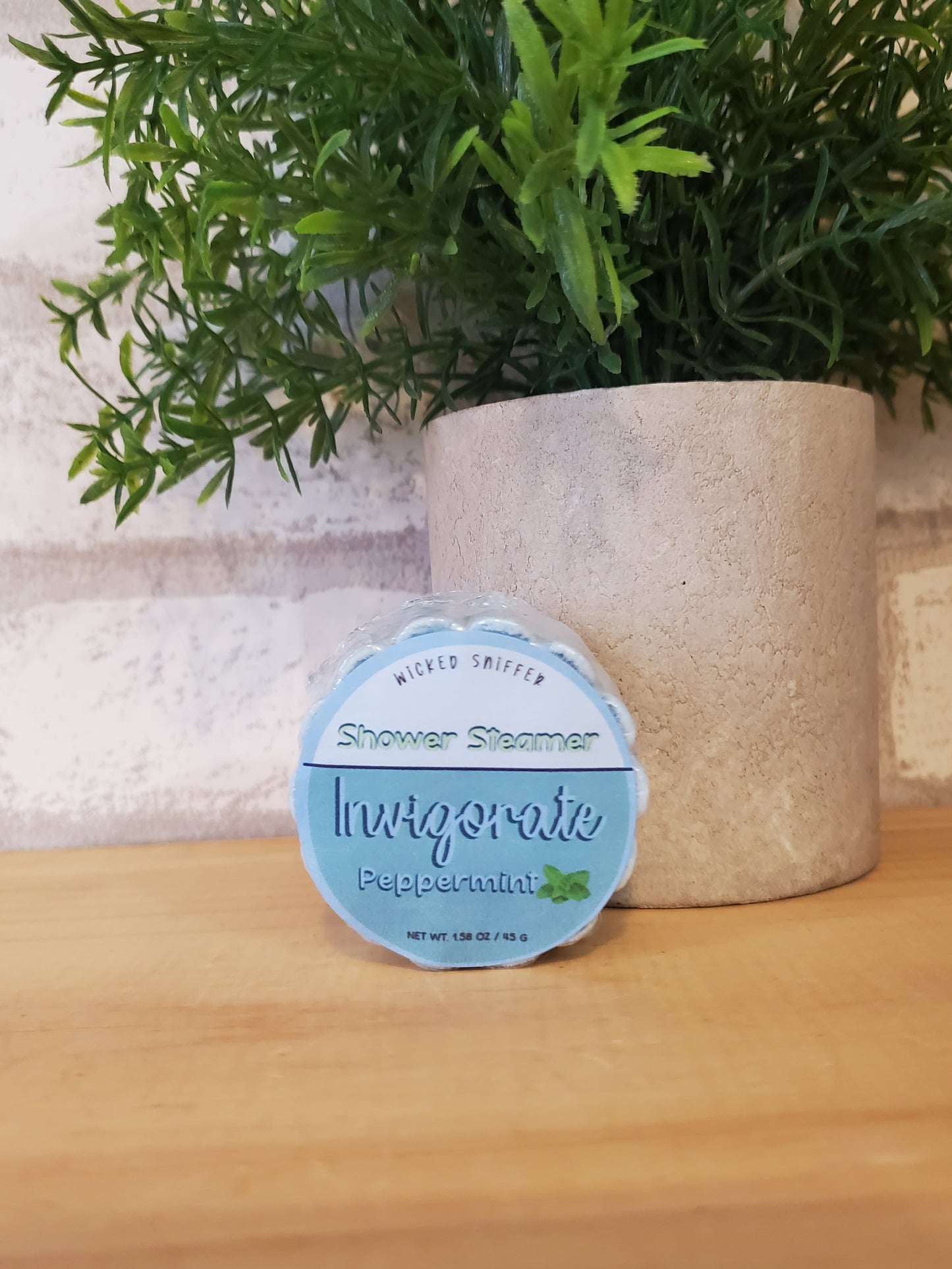 Shower steamer with a label on a wooden surface next to a plant