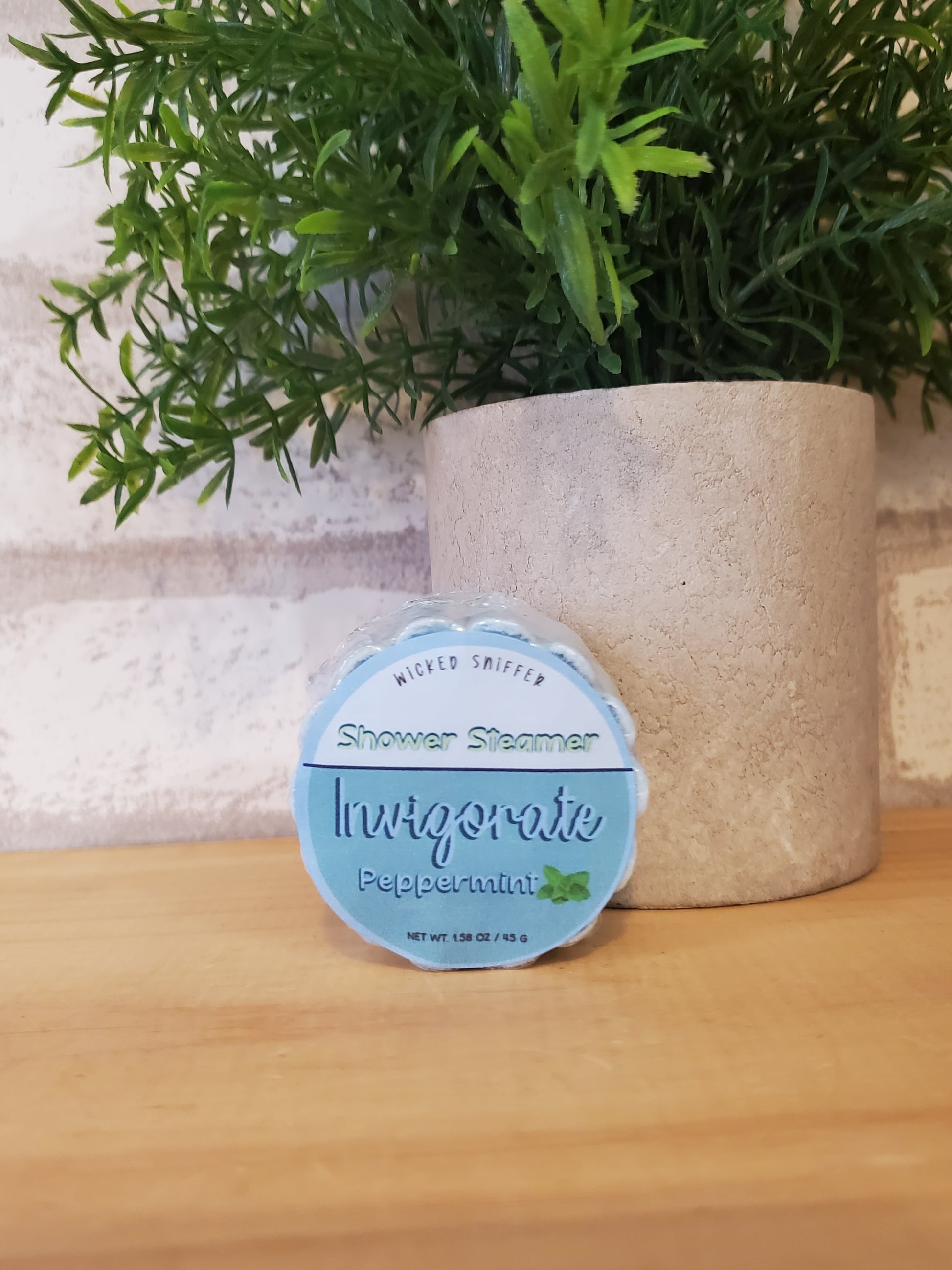 Shower steamer with a label on a wooden surface next to a plant