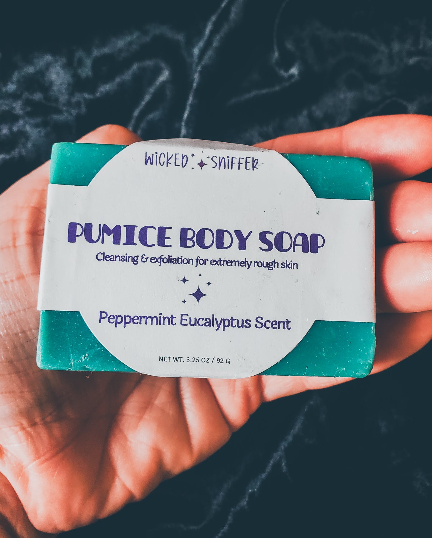 Hand holding a blue soap with a white label on a black background